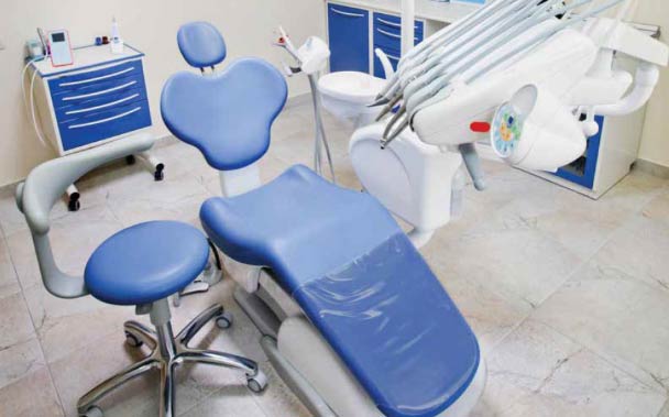 A dentist's treatment room with a modern & ergonomic chair, commonly used dental instruments in reach, a cabinet and a wheeled cabinet.
